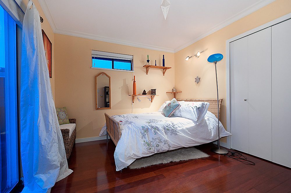 Bright bedroom with hardwood floors, twin beds, and a blue floor lamp. - 1119 Keith Road, West Vancouver