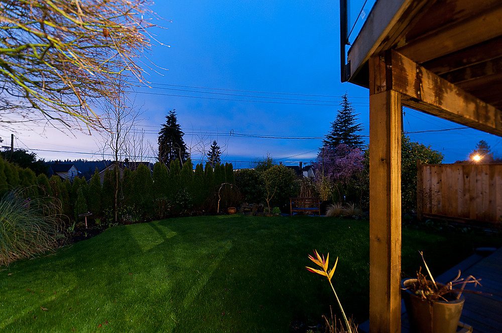 Furnished backyard with wooden deck and lush greenery, dusk sky above. - 1119 Keith Road, West Vancouver