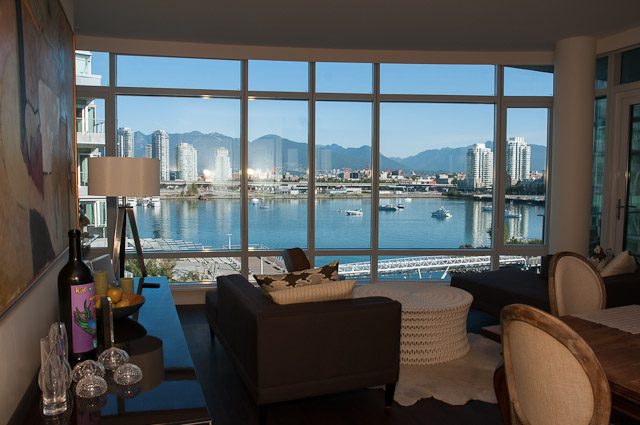 Bright living room with a stunning city view and waterfront access, featuring a large window and comfortable seating.