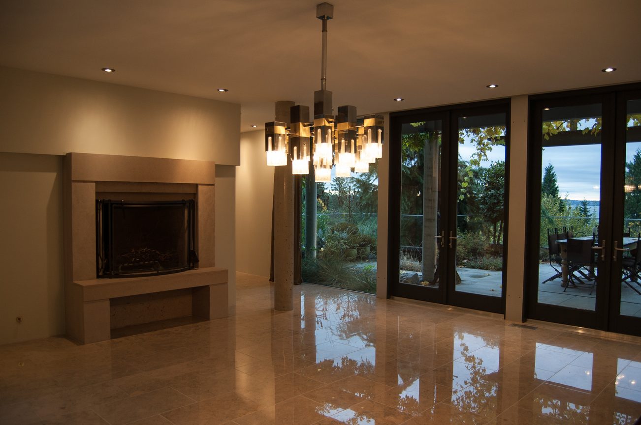 Spacious living room with fireplace, modern chandelier, and glass doors leading to outdoor garden. - 4454 Regency Place, West Vancouver