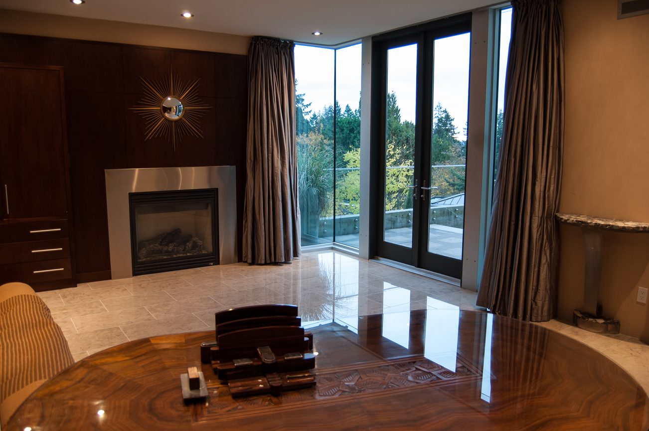 Spacious living room with large windows, hardwood floors, and a modern fireplace. - 4454 Regency Place, West Vancouver
