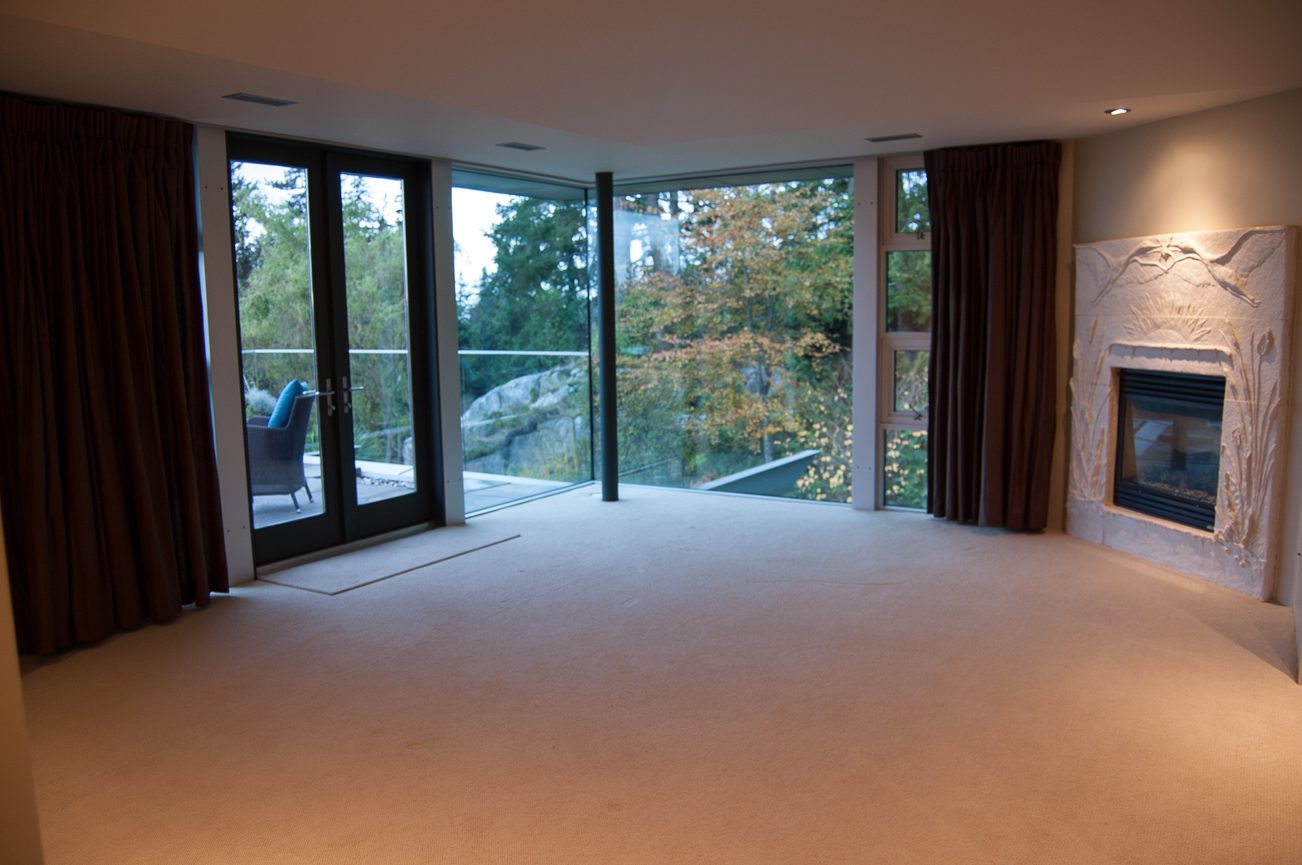 Spacious living room with large windows, fireplace, and view of trees. - 4454 Regency Place, West Vancouver