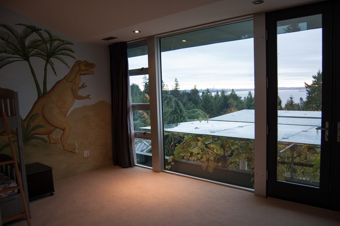 Bright living room with large windows, city view, and dinosaur mural. - 4454 Regency Place, West Vancouver