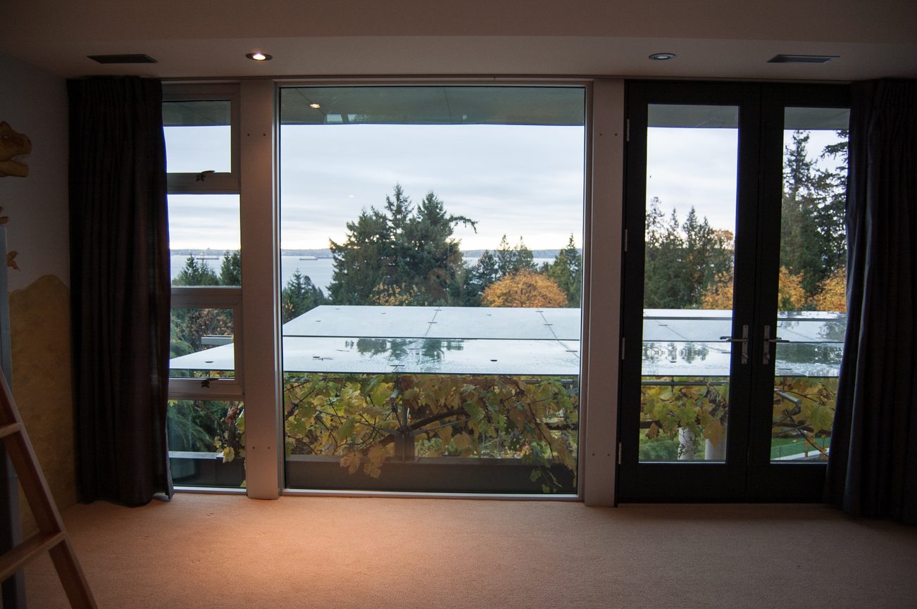 Bright living room with large windows offering a scenic view of the waterfront and trees. - 4454 Regency Place, West Vancouver