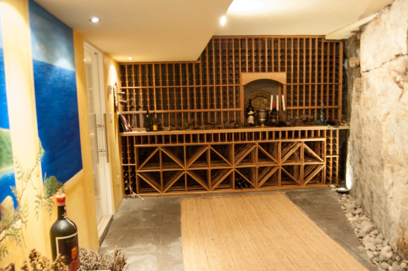 Furnished wine cellar with wooden racks and stone wall. - 4454 Regency Place, West Vancouver