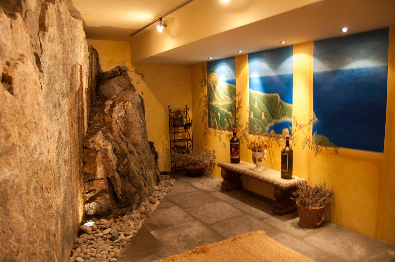 Furnished living room with stone wall, mural, and wine bottles. - 4454 Regency Place, West Vancouver