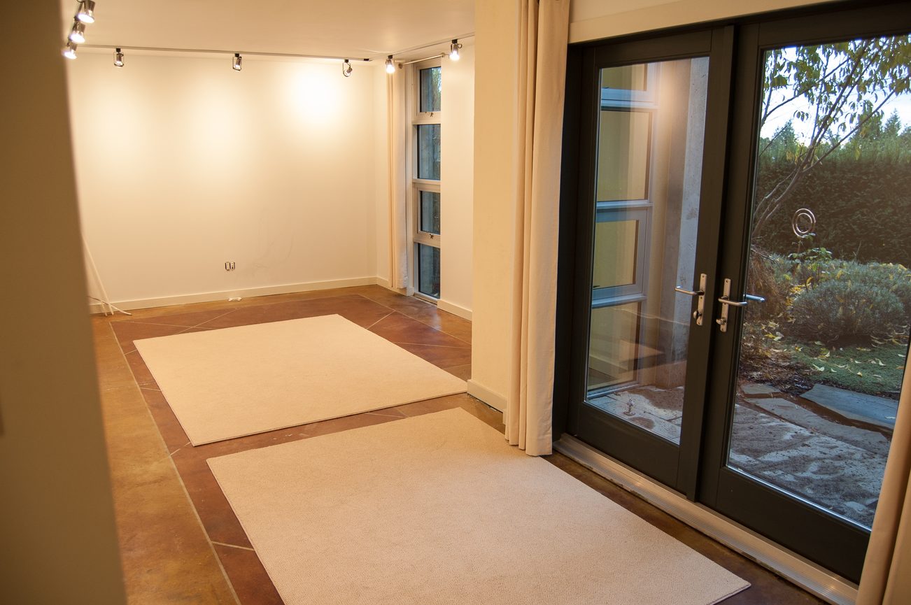 Bright living room with sliding glass doors leading to a garden, featuring a large area rug and track lighting. - 4454 Regency Place, West Vancouver
