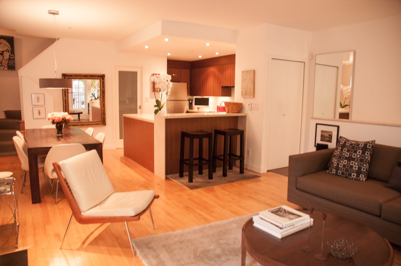 Bright kitchen with wooden cabinets, hardwood floors, and a cozy living area with a coffee table and modern furniture.