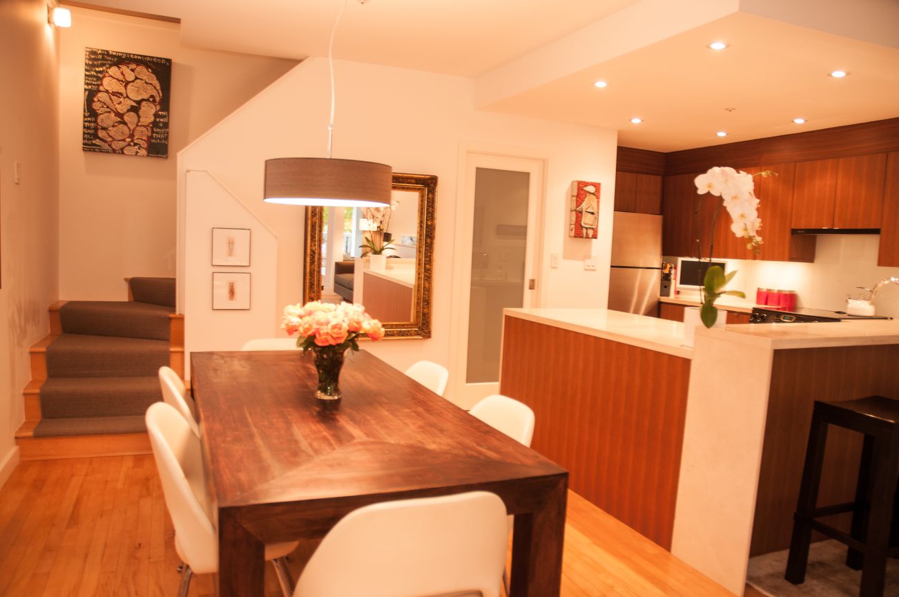 Bright dining area with wooden table, white chairs, and a kitchen in the background. - 7-2305 West 10th Ave, Vancouver West Side