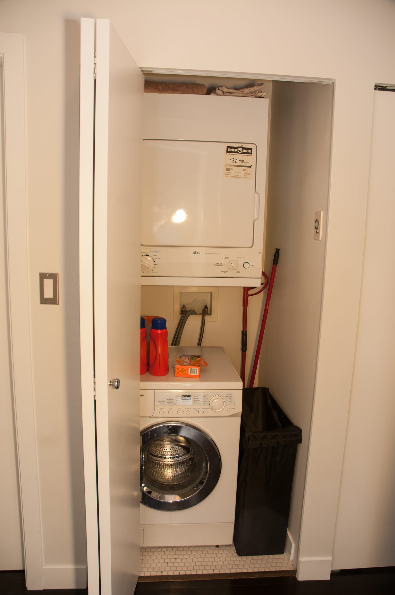 Compact laundry room with stacked washer and dryer, red broom, and orange detergent bottle. - 1406-1050 Smithe, Vancouver Downtown