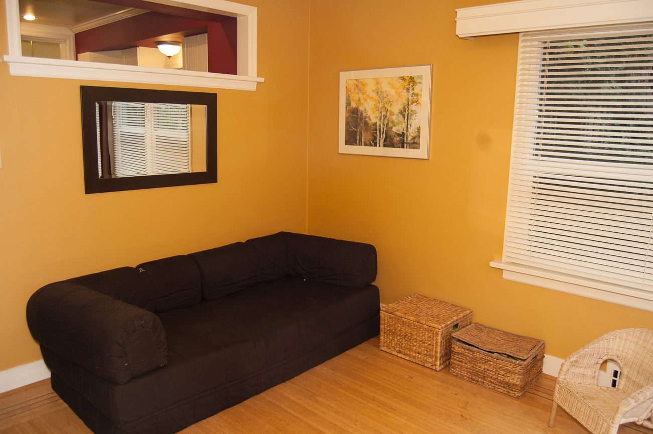 Furnished living room with black sectional sofa, wooden floors, and framed artwork. - 139 Osbourne Rd. East, North Vancouver
