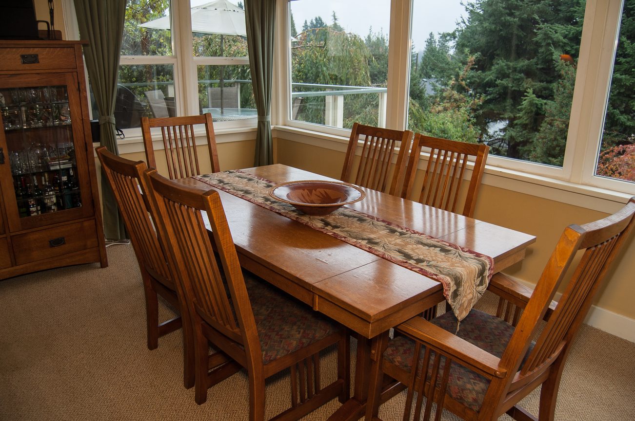 Furnished dining area with wooden table, chairs, and large windows showing a scenic view. - 139 Osbourne Rd. East, North Vancouver
