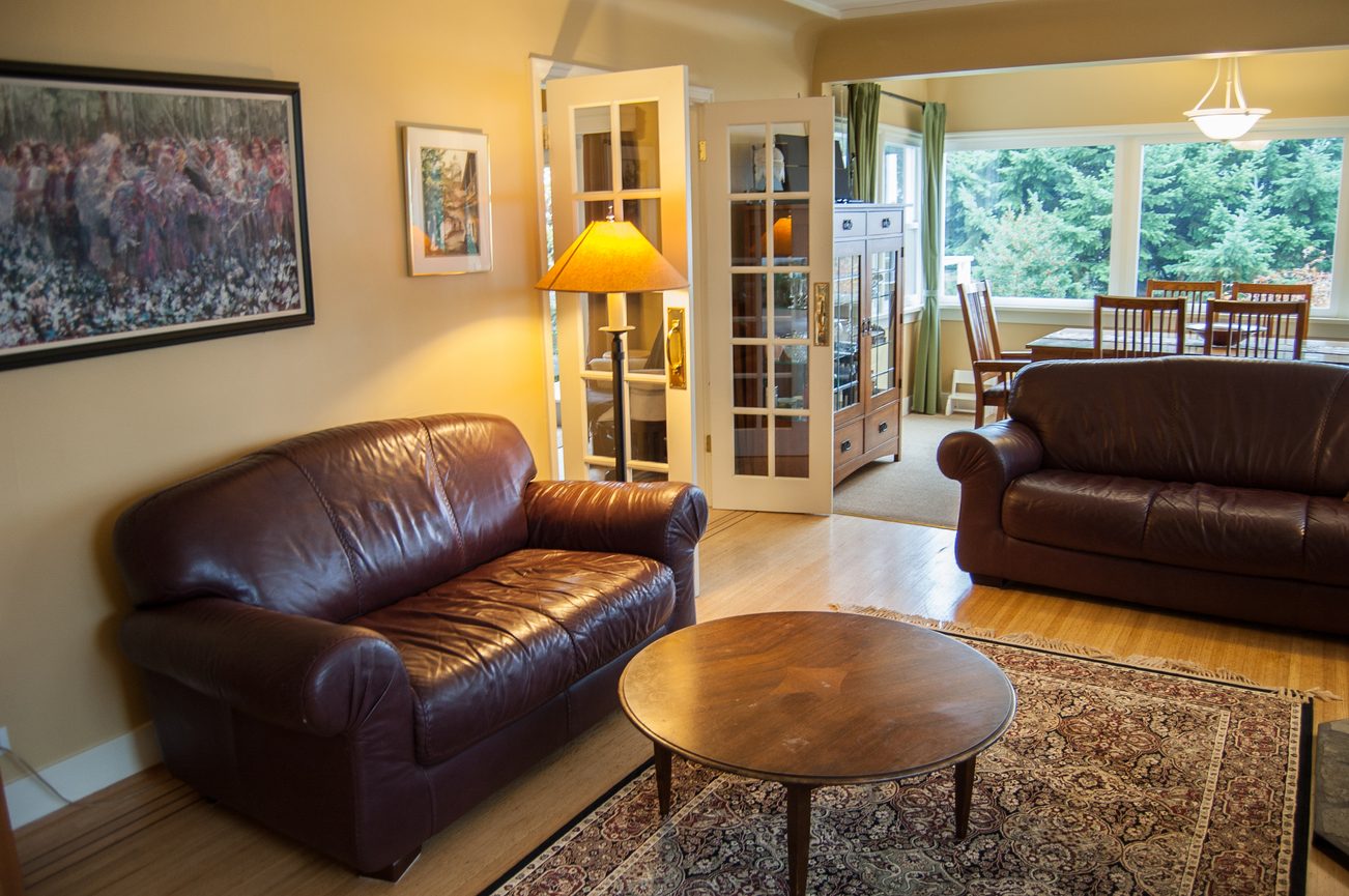 Furnished living room with leather sofas, hardwood floors, and a view of greenery outside. - 139 Osbourne Rd. East, North Vancouver