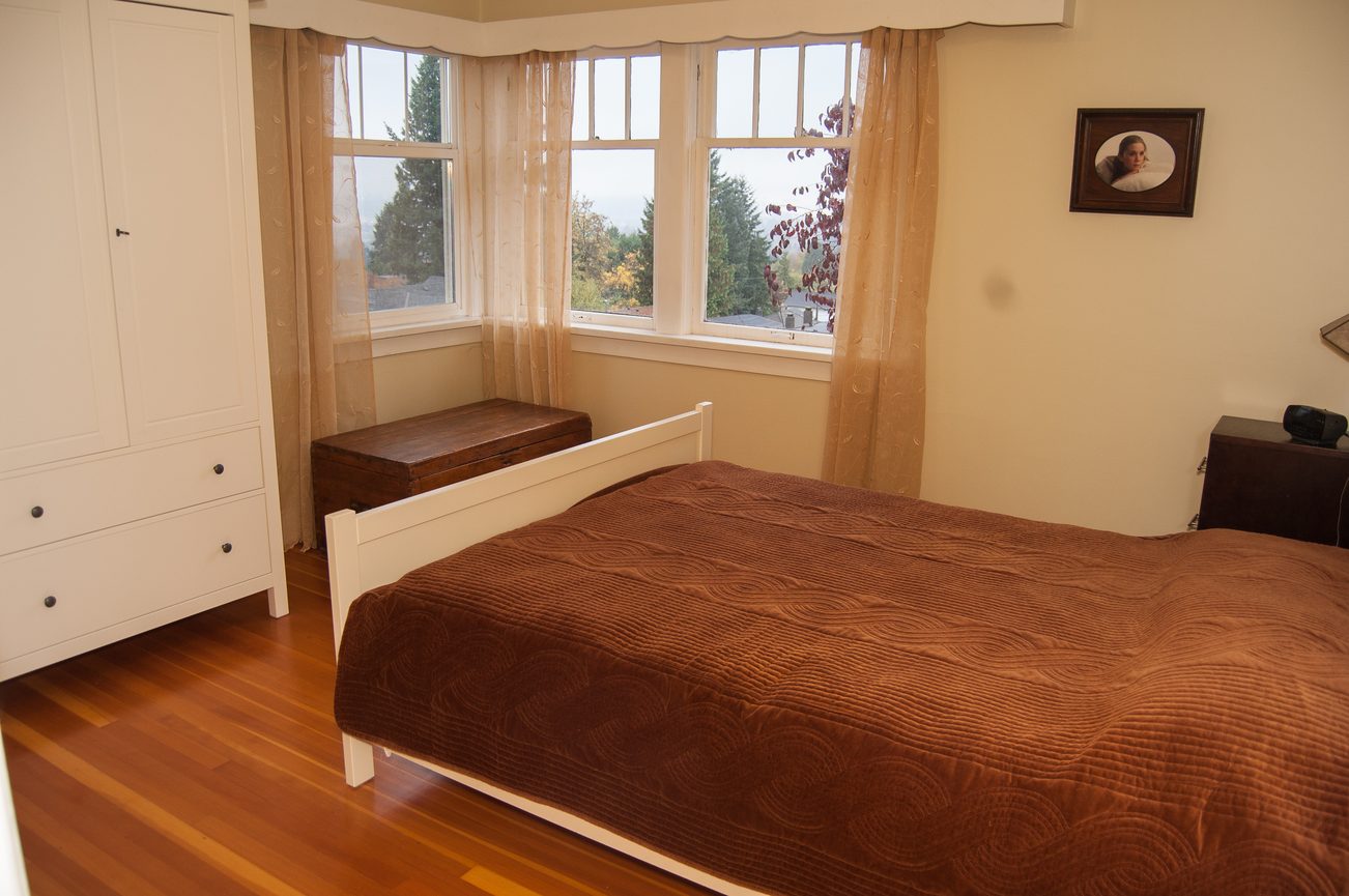 Bright bedroom with bay window, hardwood floors, and brown bedding. - 139 Osbourne Rd. East, North Vancouver