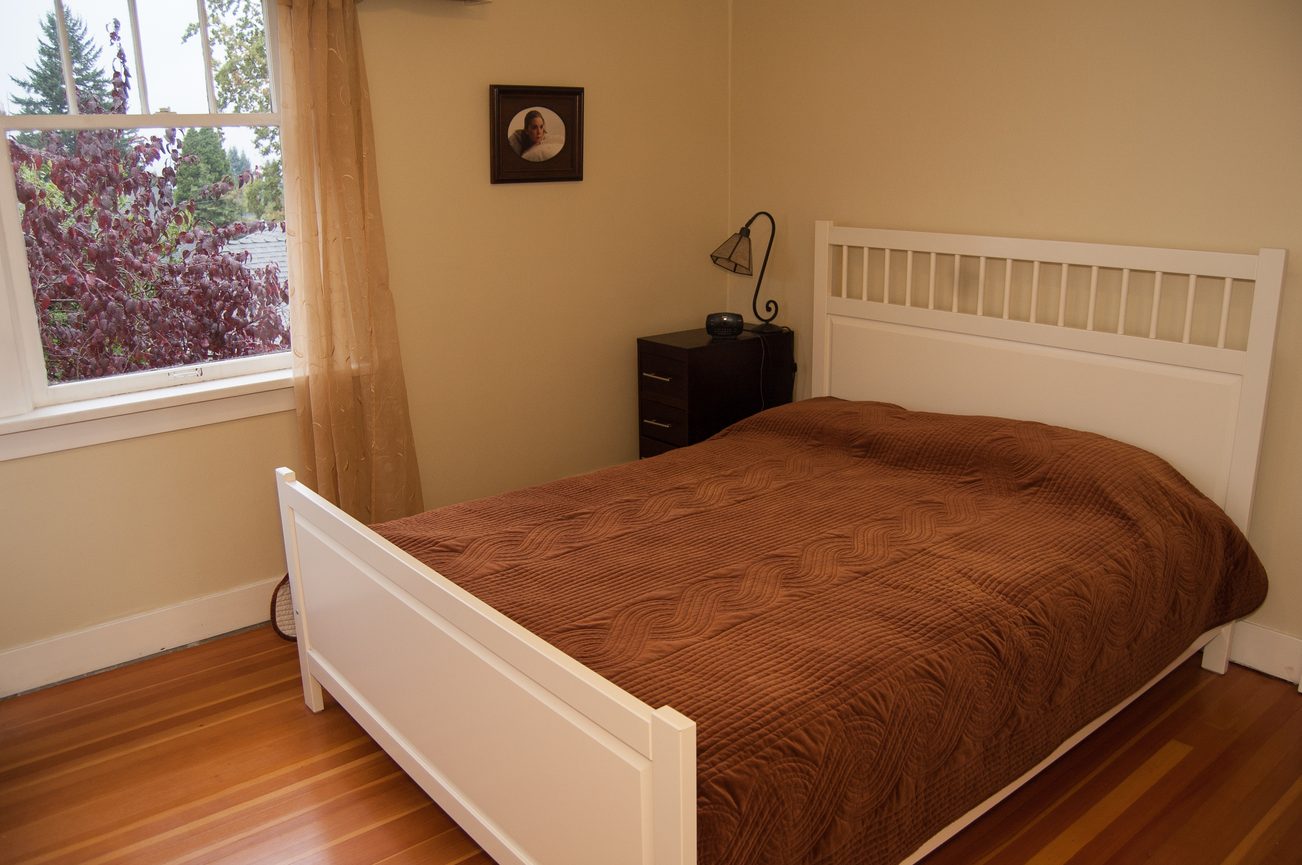 Bright bedroom with white bed frame, hardwood floors, and a window view of trees. - 139 Osbourne Rd. East, North Vancouver
