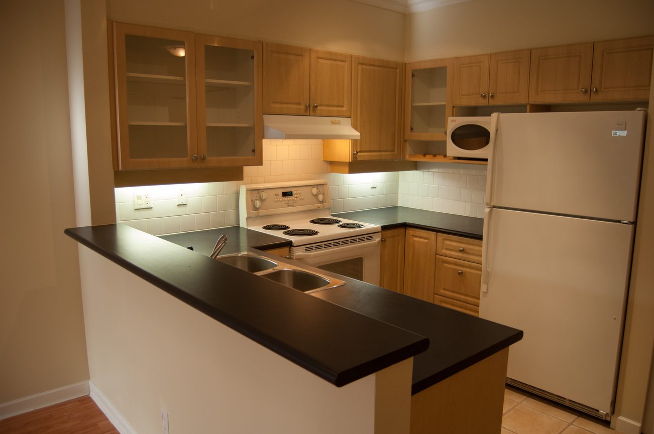 Bright kitchen with black countertops, light wood cabinets, and a white stove. - 232 - 3629 Deercrest Dr, North Vancouver