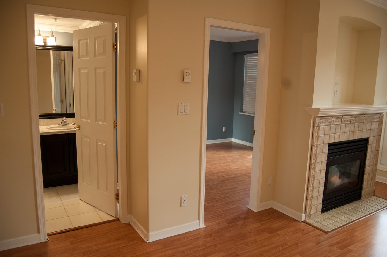 Bright living room with hardwood floors and a fireplace, leading to a bathroom with a vanity and mirror. - 232 - 3629 Deercrest Dr, North Vancouver