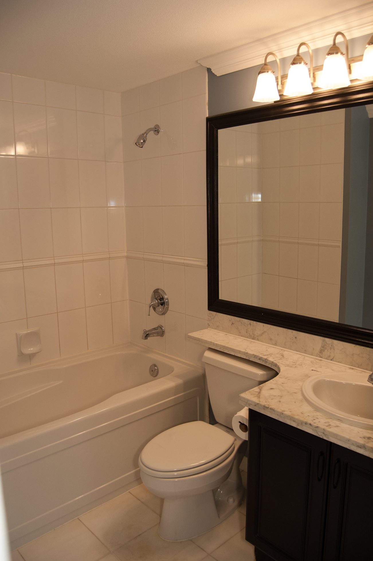 Bathroom with white tile, marble countertop, and black-framed mirror. - 232 - 3629 Deercrest Dr, North Vancouver