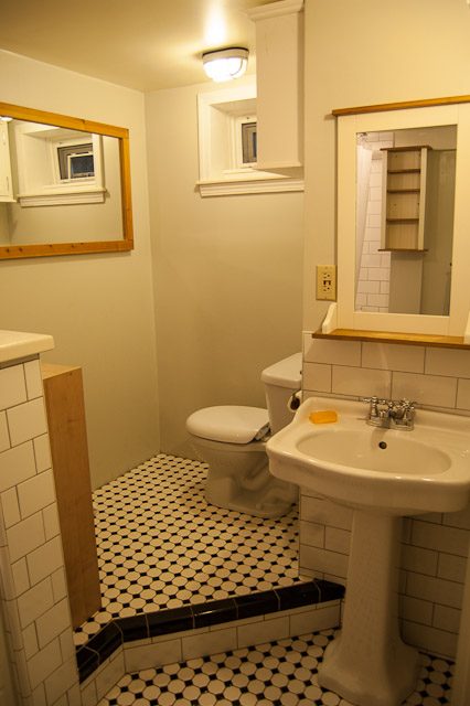 Small bathroom with black-and-white checkered floor, white sink, and wooden accents. - 139 Osbourne Rd. East, North Vancouver