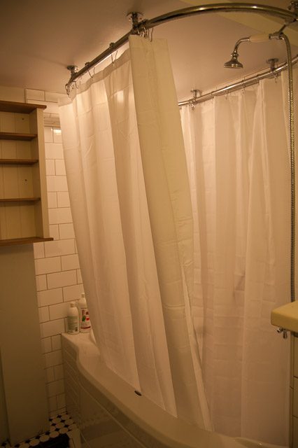 Bathroom with white shower curtain and curved rod, wooden shelf visible. - 139 Osbourne Rd. East, North Vancouver