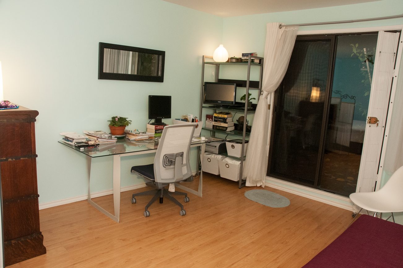 Bright and cozy home office with hardwood floors, glass desk, and sliding glass door leading to a patio. - 104 - 575 W 13th Ave, Vancouver West Side
