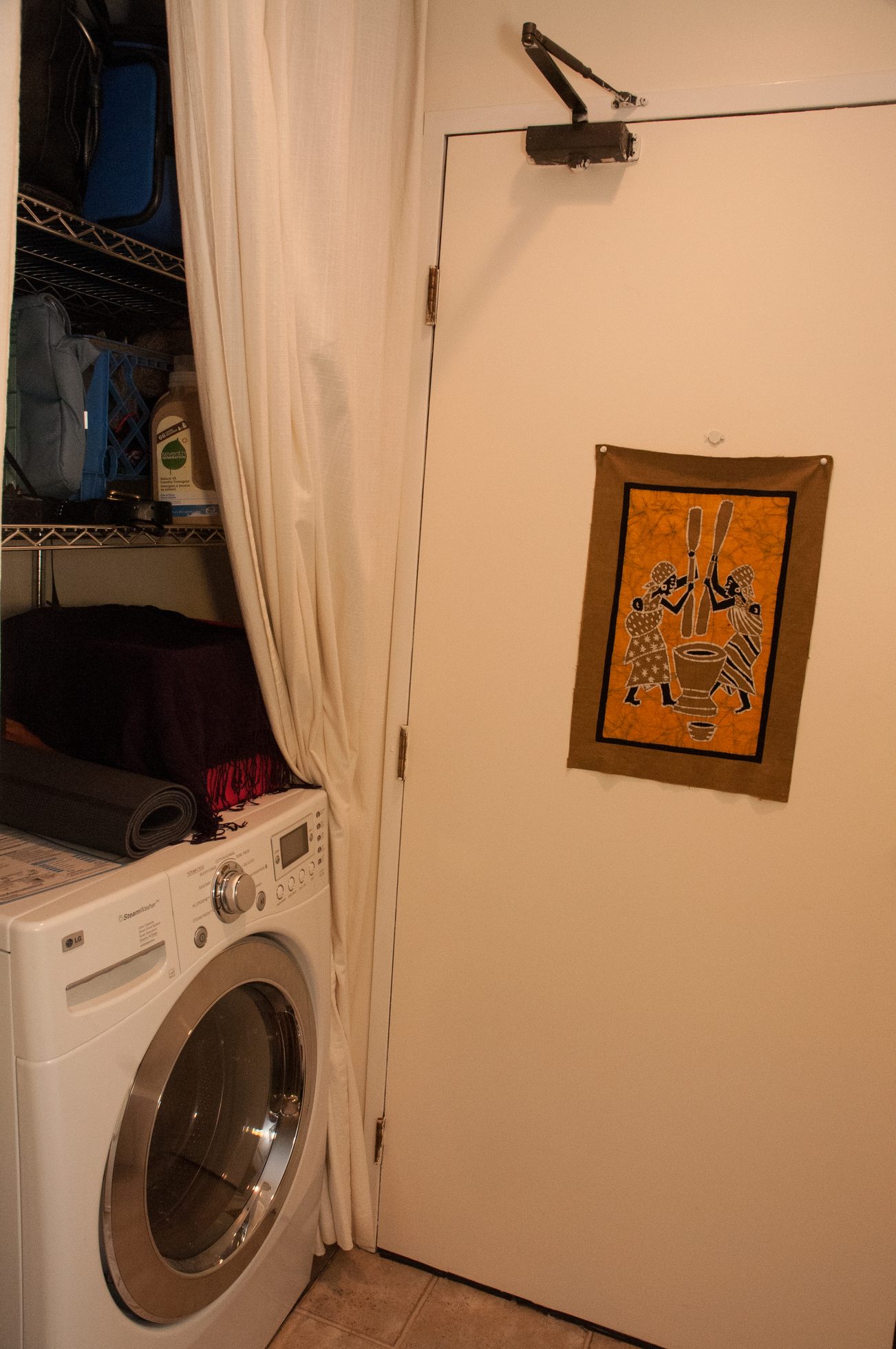 Laundry room with orange artwork, white washing machine, and storage shelves. - 104 - 575 W 13th Ave, Vancouver West Side
