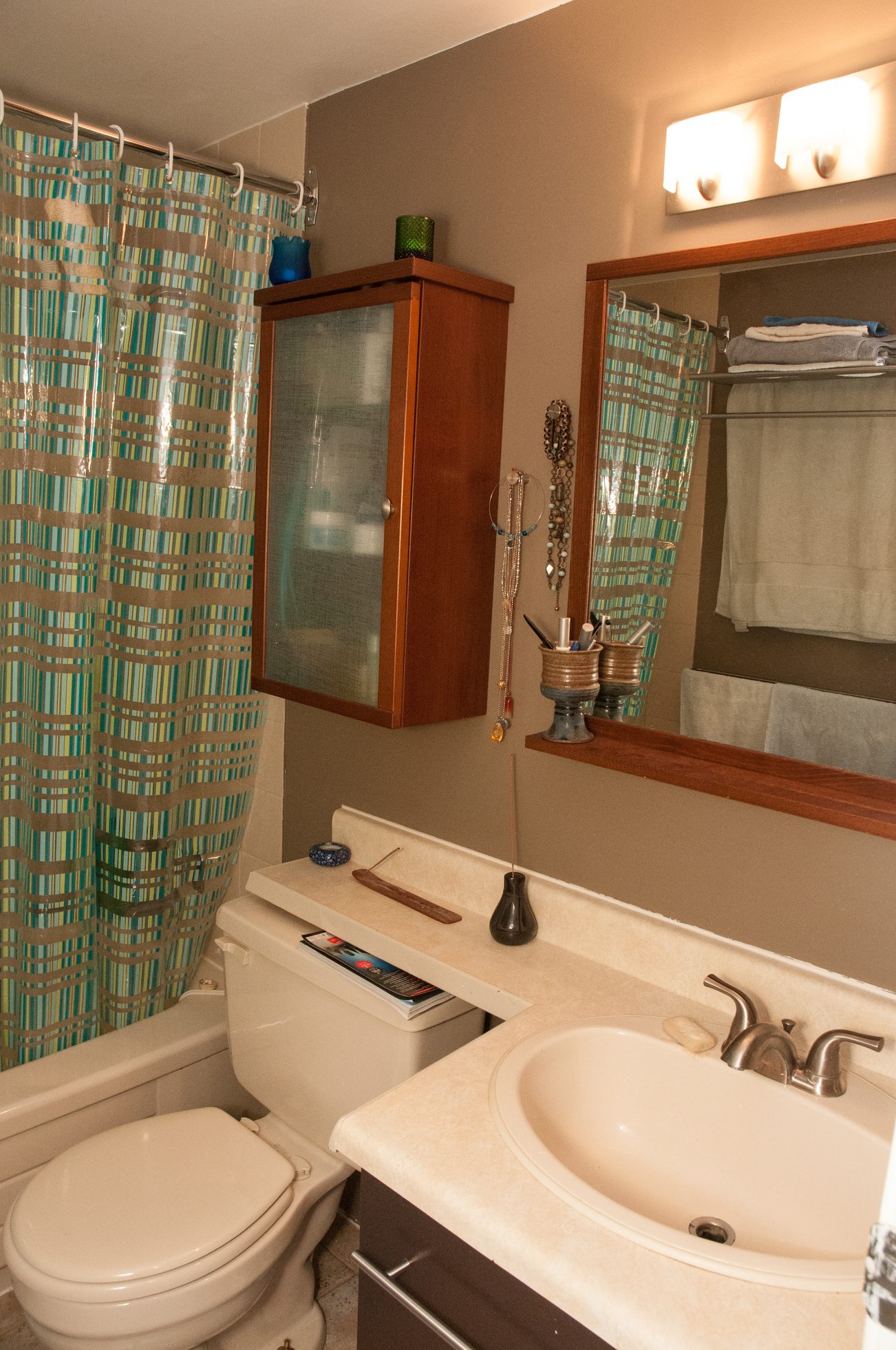 Furnished bathroom with beige countertop, wooden cabinet, and striped shower curtain. - 104 - 575 W 13th Ave, Vancouver West Side