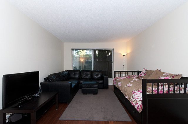 Furnished living room with black leather couches and floral patterned rug. - 106-827 West 16th Street, North Vancouver
