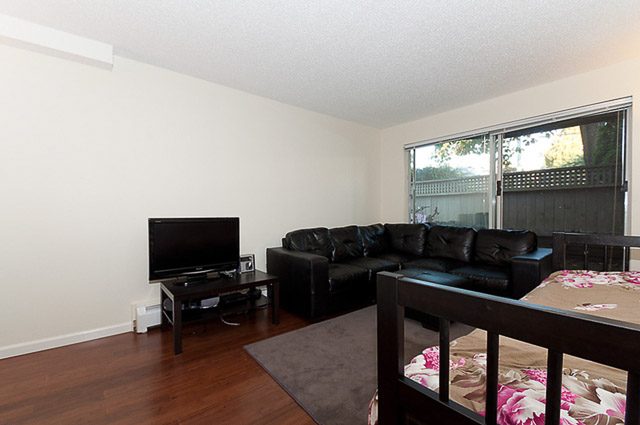 Living room with hardwood floors and a large window. - 106-827 West 16th Street, North Vancouver