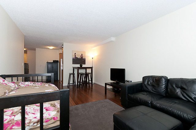 Furnished living room with black leather couches and hardwood floors. - 106-827 West 16th Street, North Vancouver