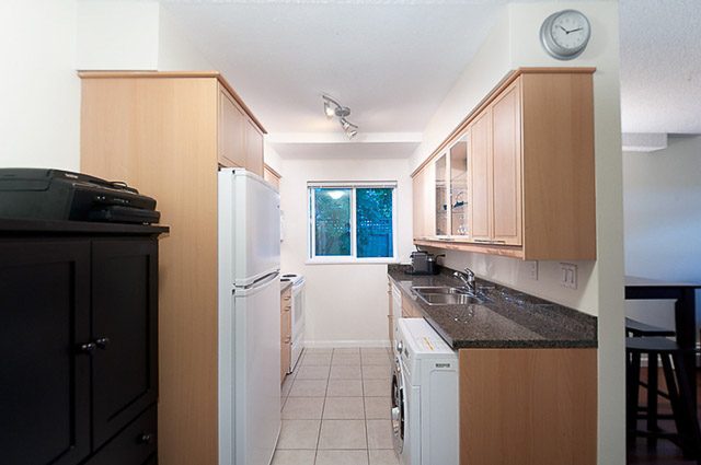 Bright kitchen with granite countertops and a city view through sliding doors. - 106-827 West 16th Street, North Vancouver