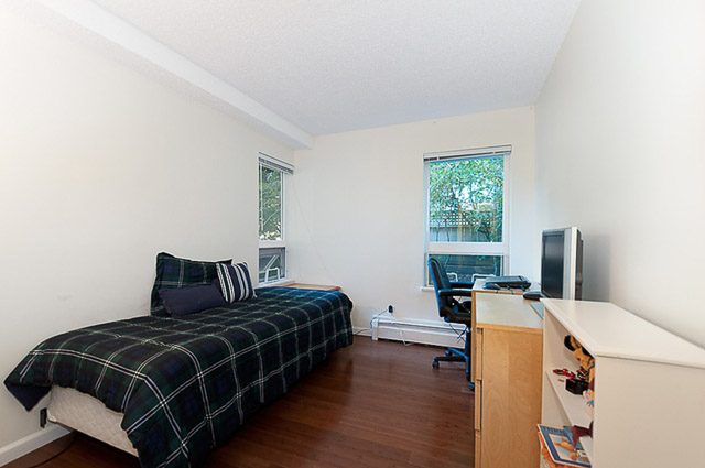 Bright bedroom with plaid bedding and hardwood floors. - 106-827 West 16th Street, North Vancouver
