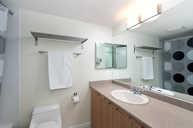 Bright bathroom with modern sink, countertop, and large mirror. - 106-827 West 16th Street, North Vancouver