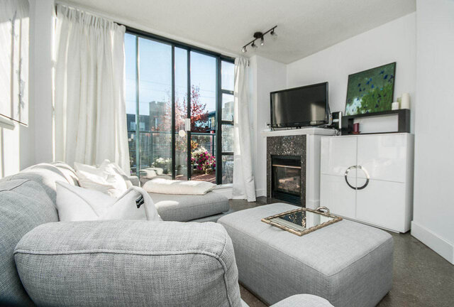 Spacious living room with large windows, modern fireplace, and cozy grey furniture. - 312 - 1630 West 1st Ave., Vancouver West Side