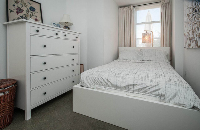 Spacious 1-bedroom condo with a cozy, minimalist bedroom featuring a white dresser, a neatly made bed, and a large window...