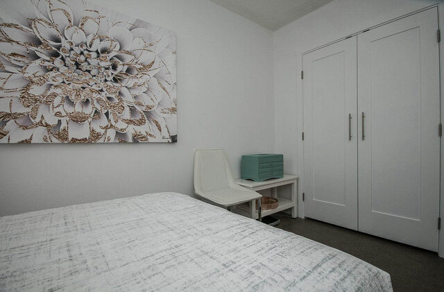 Spacious bedroom with a large floral artwork and a white wardrobe, featuring a cozy bed and a nightstand with a teal box.
