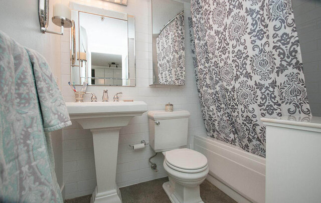Furnished bathroom with white pedestal sink, patterned shower curtain, and teal towels. - 312 - 1630 West 1st Ave., Vancouver West Side