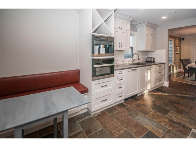 Bright kitchen with white cabinets, dark stone countertops, and a red cushioned bench. - 14 West 13th Ave, Vancouver East Side