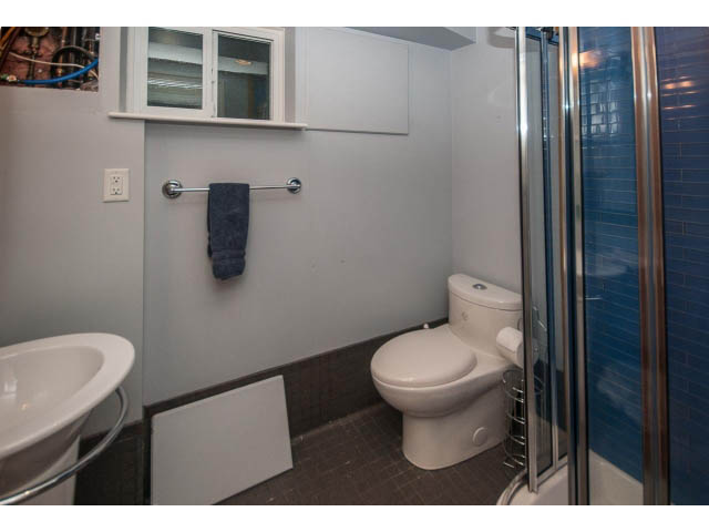 Bathroom with white sink, toilet, and blue-tiled shower. - 14 West 13th Ave, Vancouver East Side