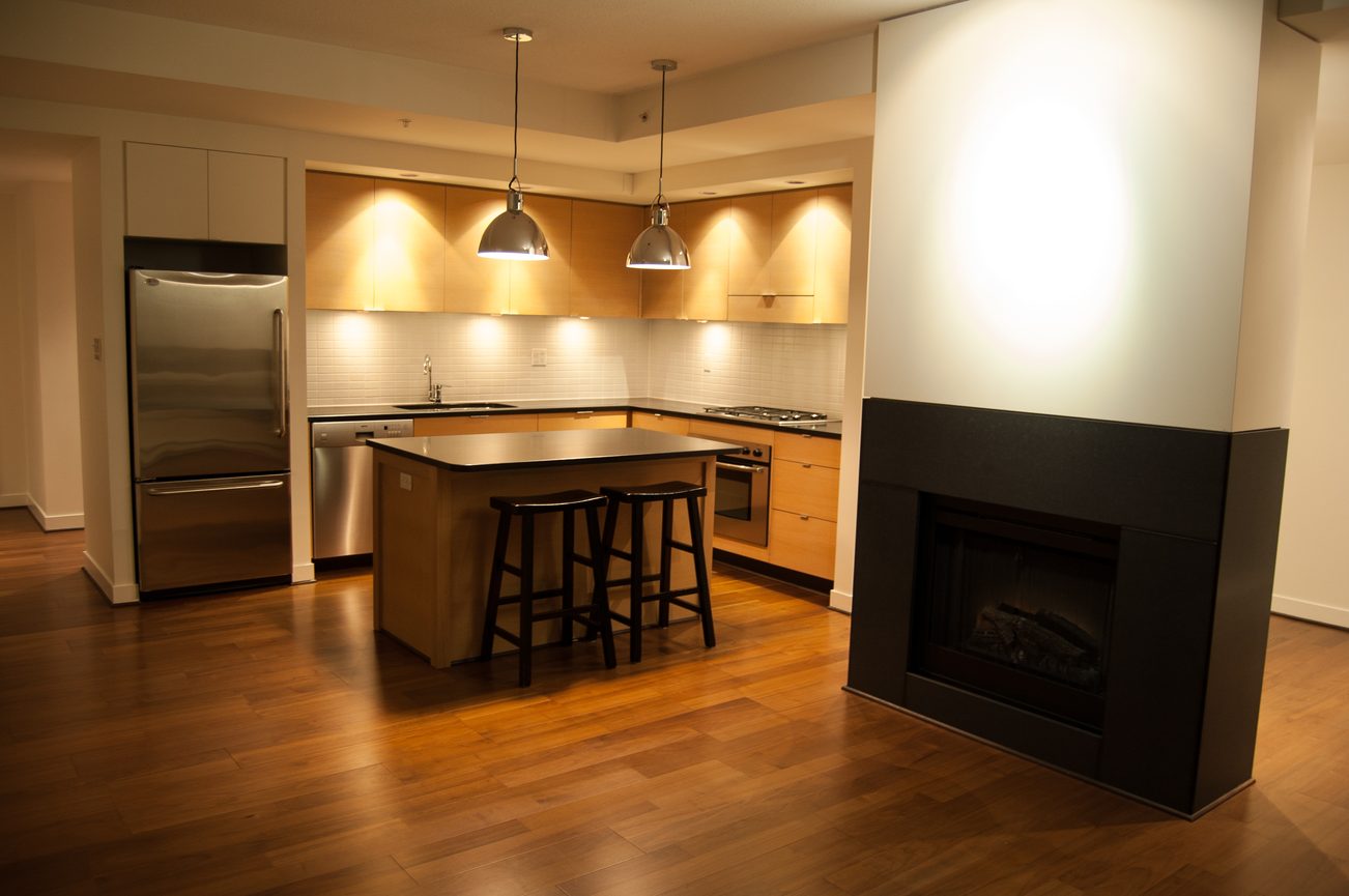 Bright kitchen with modern stainless steel appliances and wooden cabinetry, featuring a central island and hardwood floors.