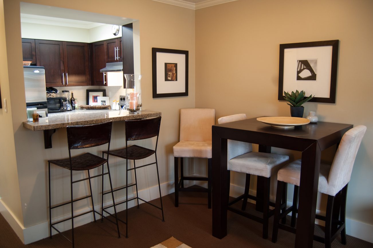 Furnished dining area with dark wood table and chairs, adjacent to a kitchen with granite countertops and bar stools.