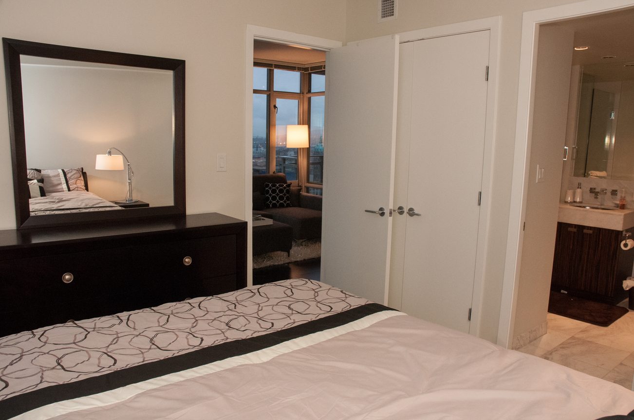 Spacious bedroom with mirrored dresser, city view, and modern furnishings. - 2306-788 Richards, Vancouver Downtown
