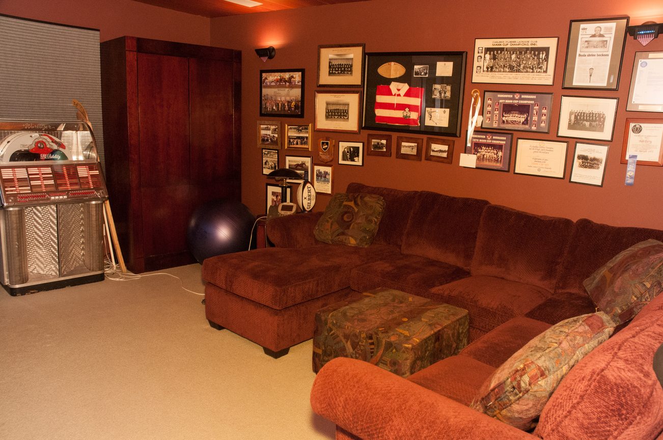 Living room with vintage jukebox, sports memorabilia on wall, and sectional couch. - 829 Younette Drive, West Vancouver