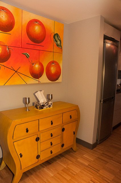Bright kitchen with yellow dresser, orange artwork, hardwood floors, stainless steel fridge. - 506-128 West Cordova St, Vancouver Downtown