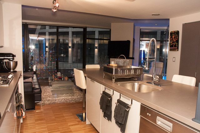 Modern open-concept living space with sleek countertops and hardwood floors, featuring a city view through large windows.