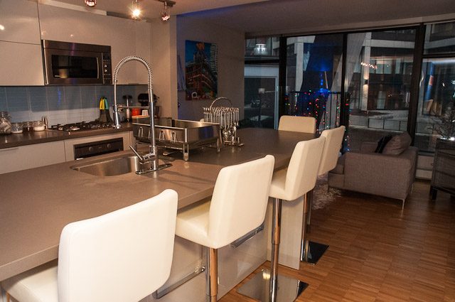 Modern kitchen with sleek countertops and hardwood floors, featuring a city view through large windows. - 506-128 West Cordova St, Vancouver Downtown