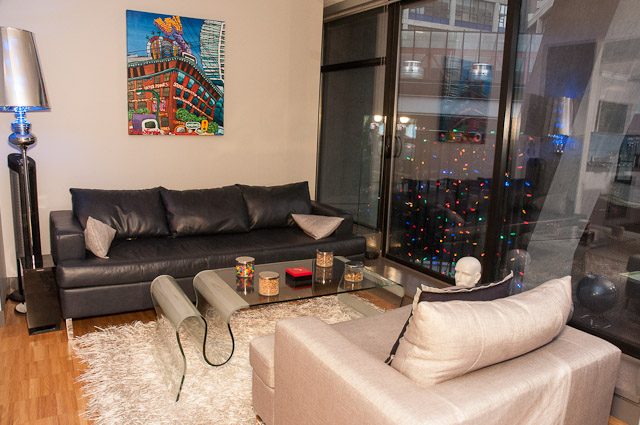 Furnished living room with a leather couch, hardwood floors, and a city view through sliding glass doors.