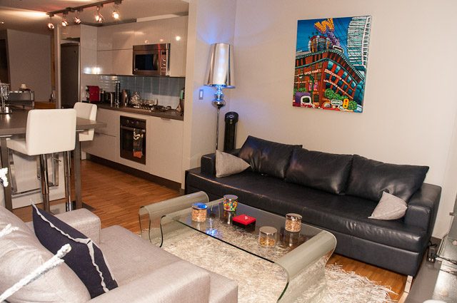 Bright living room with modern decor, colorful artwork, and sleek kitchen in the background. - 506-128 West Cordova St, Vancouver Downtown