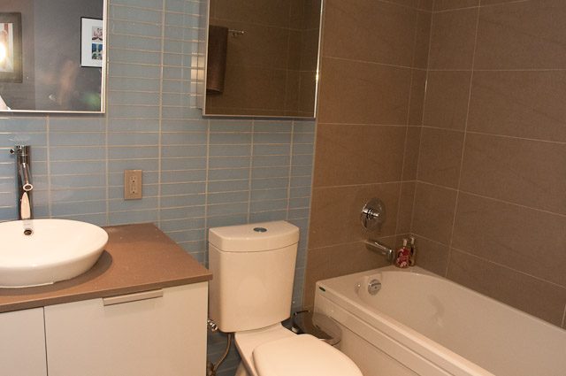 Modern bathroom with light blue tiles and beige walls, featuring a sink, toilet, and bathtub. - 506-128 West Cordova St, Vancouver Downtown