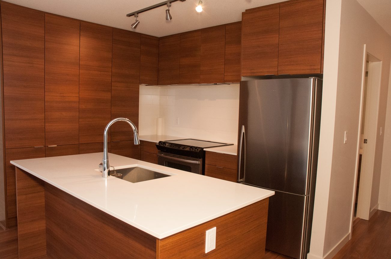 Bright kitchen with modern white countertops and dark wood cabinets, featuring a stainless steel refrigerator and a sleek...